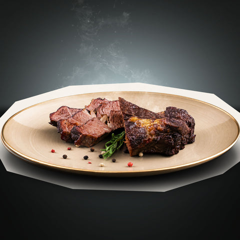 Saftige Scheiben des „Beef Royal“-Steaks „Special Cut vom Rinderrücken“ von AUMAERK sind auf einem beigen Teller angerichtet, garniert mit Rosmarin und Pfefferkörnern, vor einem dunklen Hintergrund mit Farbverlauf, aus dem leichter Dampf aufsteigt.