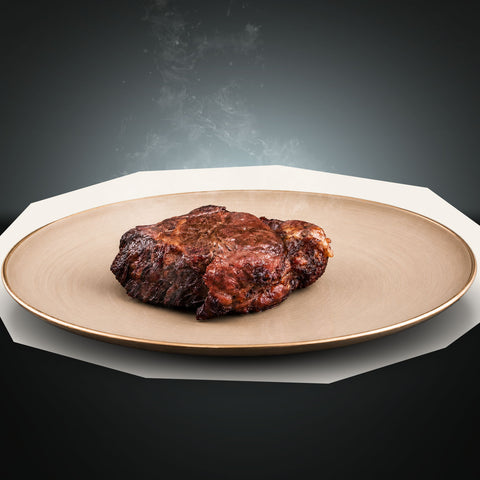 Ein frisch zubereitetes AUMAERK Special Cut vom Rinderrücken „Beef Royal“-Steak liegt auf einem runden, beigen Teller mit goldenem Rand, während vor einem dunklen Hintergrund mit Farbverlauf Dampf aufsteigt.