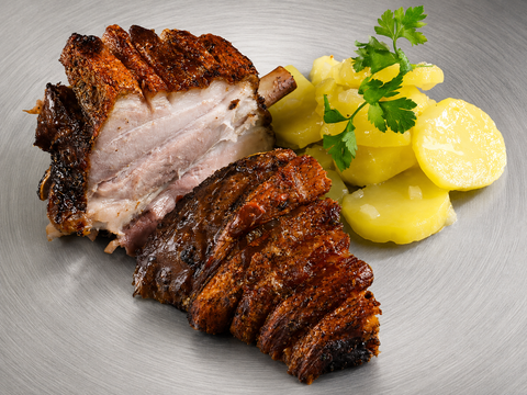 Eine Portion AUMAERK-Stelze „Crack Leg“ mit knuspriger Haut und saftigen Schichten wird neben gekochten Kartoffelscheiben, garniert mit Petersilie, auf einem silberfarbenen Teller angerichtet – perfekt zubereitet nach der AUMAERK-Methode.