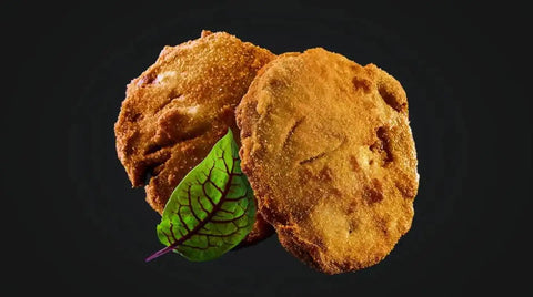 Zwei goldbraune, panierte und gebratene AUMAERK-Patties sind vor einem schwarzen Hintergrund abgebildet, davor ein kleines grünes Blatt als Garnierung.