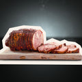 Der Kalbsrollbraten "Tender Wheel" von AUMAERK aus zartem Kalbfleisch liegt gebunden und goldbraun auf einem Holzbrett vor dunklem Hintergrund, mit dicken, appetitlich aufgeschnittenen Scheiben.