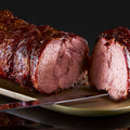 Der Kalbsrollbraten "Zartes Rad" von AUMAERK, teilweise aufgeschnitten auf einer Platte mit einem Tranchiermesser daneben, vor schwarzem Hintergrund - ideal für jedes Festtagsessen.