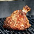 Eine knusprige Stelze "Crack Leg" von AUMAERK mit goldbraunem Crackling liegt auf einem Grillrost, perfekt zubereitet nach der AUMAERK-Methode und bereit zum Servieren.