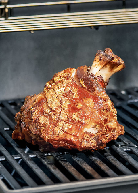 Eine knusprige Stelze "Crack Leg" von AUMAERK mit goldbraunem Crackling liegt auf einem Grillrost, perfekt zubereitet nach der AUMAERK-Methode und bereit zum Servieren.